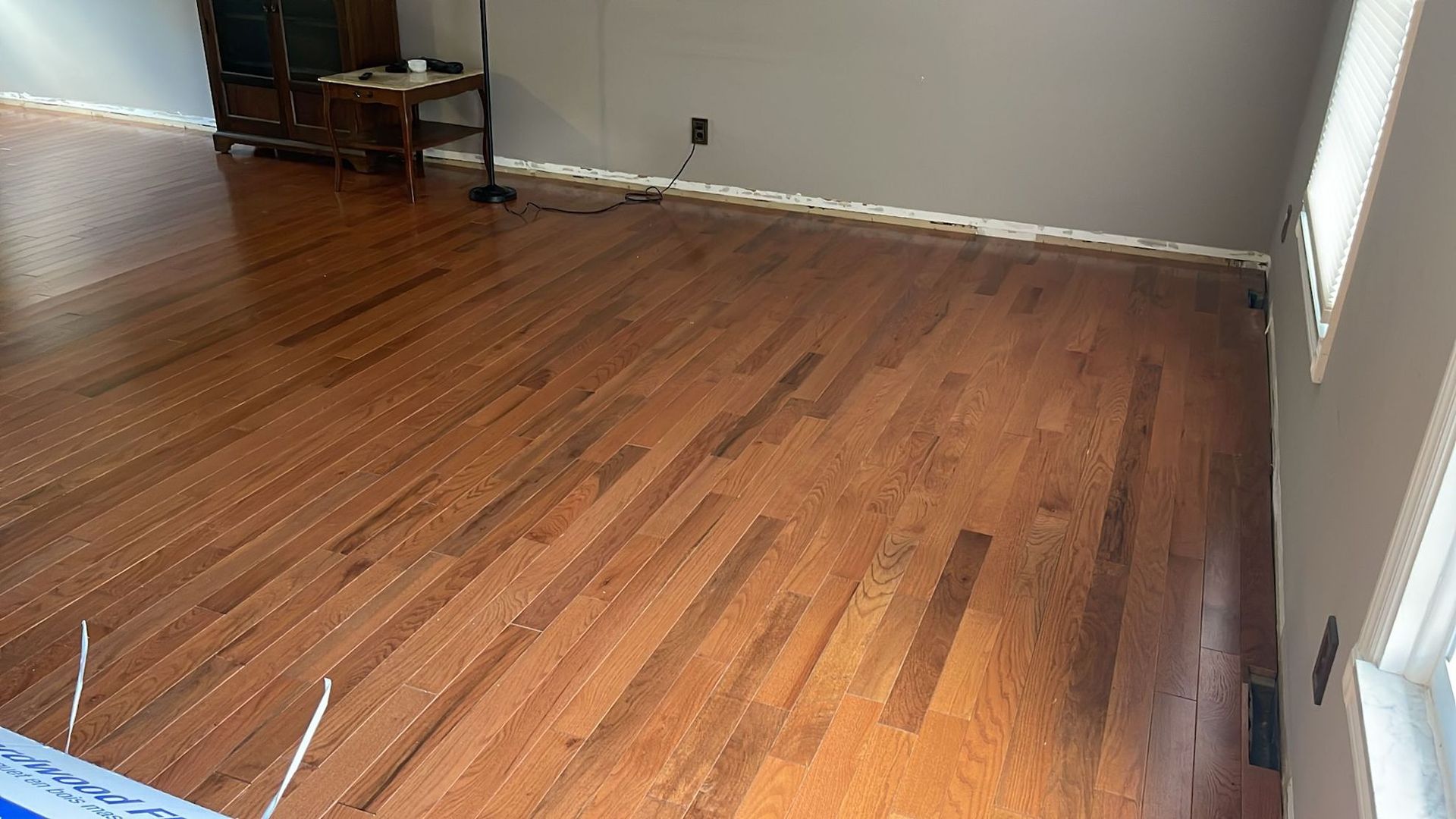 Hardwood floor in a living room; walls are gray, and there is a dark wooden cabinet.