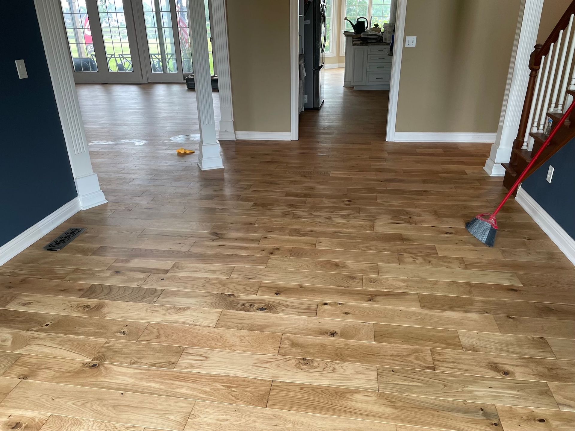 Light brown cork flooring in a home. A broom rests on the stairs, doors in the background.