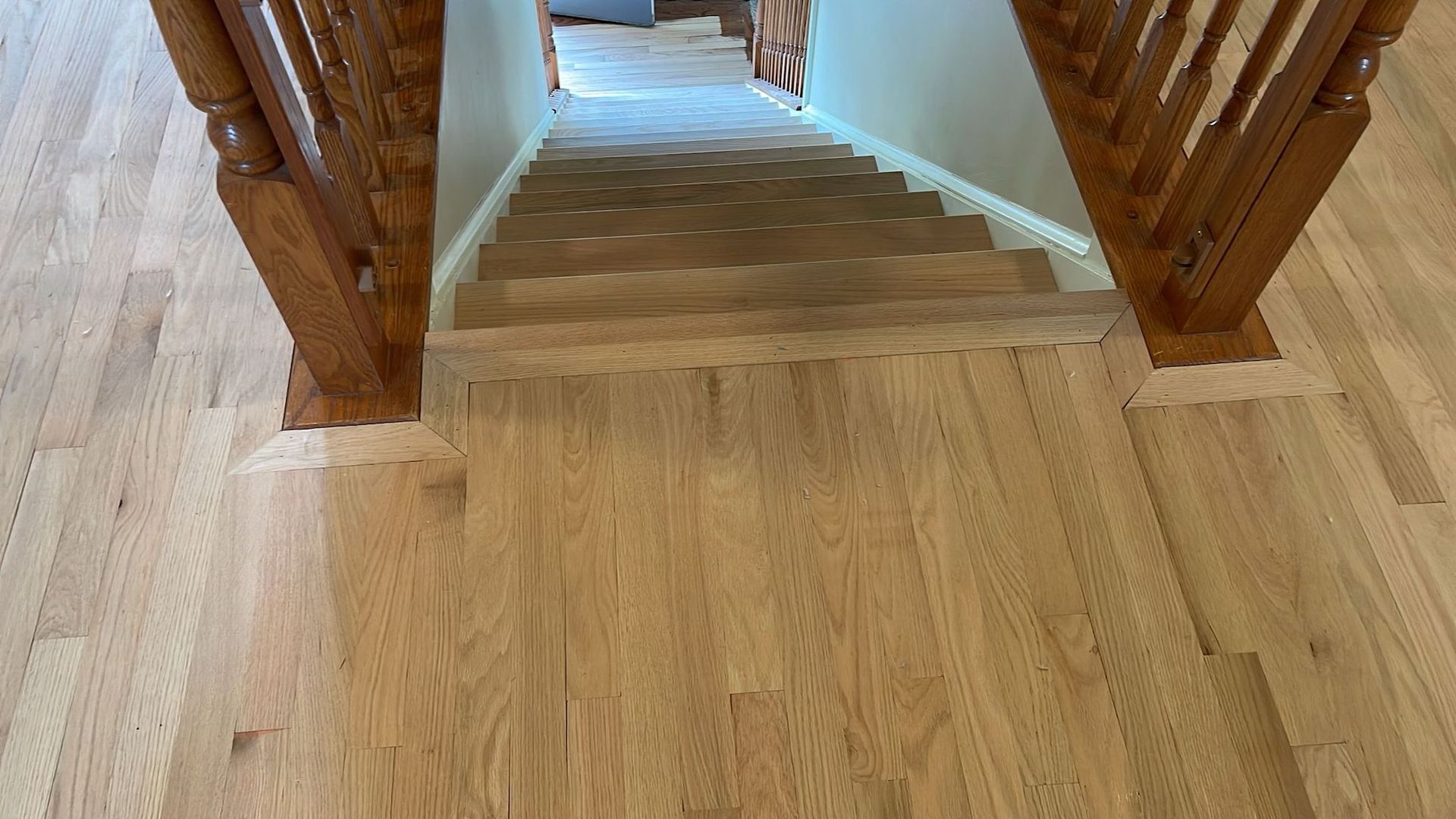 Wooden staircase with oak railings and light-colored wood flooring. The stairs lead upwards.
