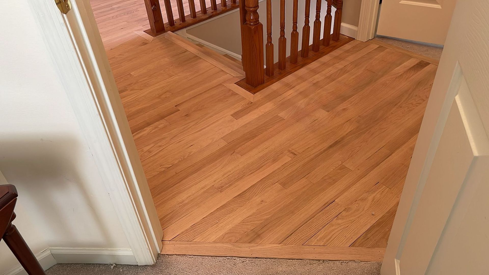 Wood floor with angled pattern, leading into a hallway with stairs.
