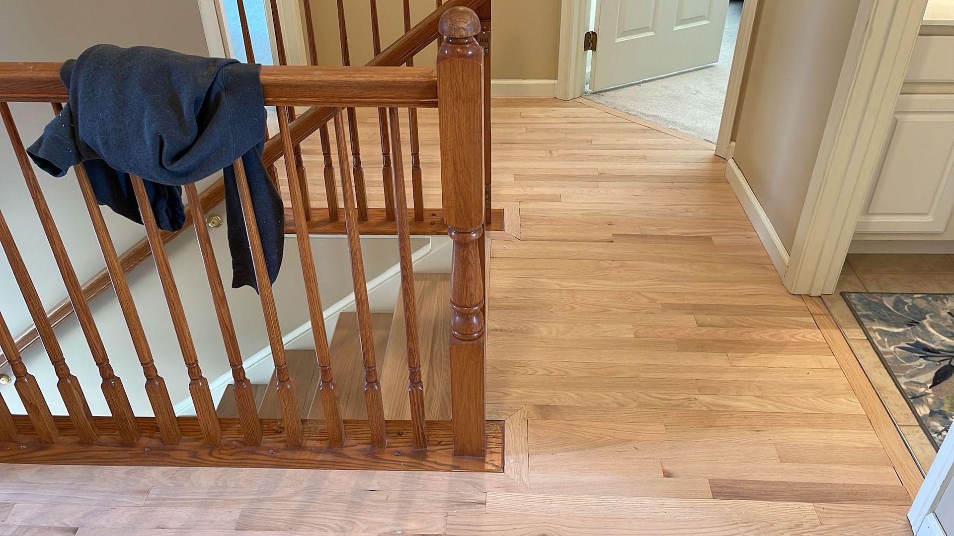 Wooden staircase with a blue jacket draped on the railing, leading to a hallway with wooden flooring.