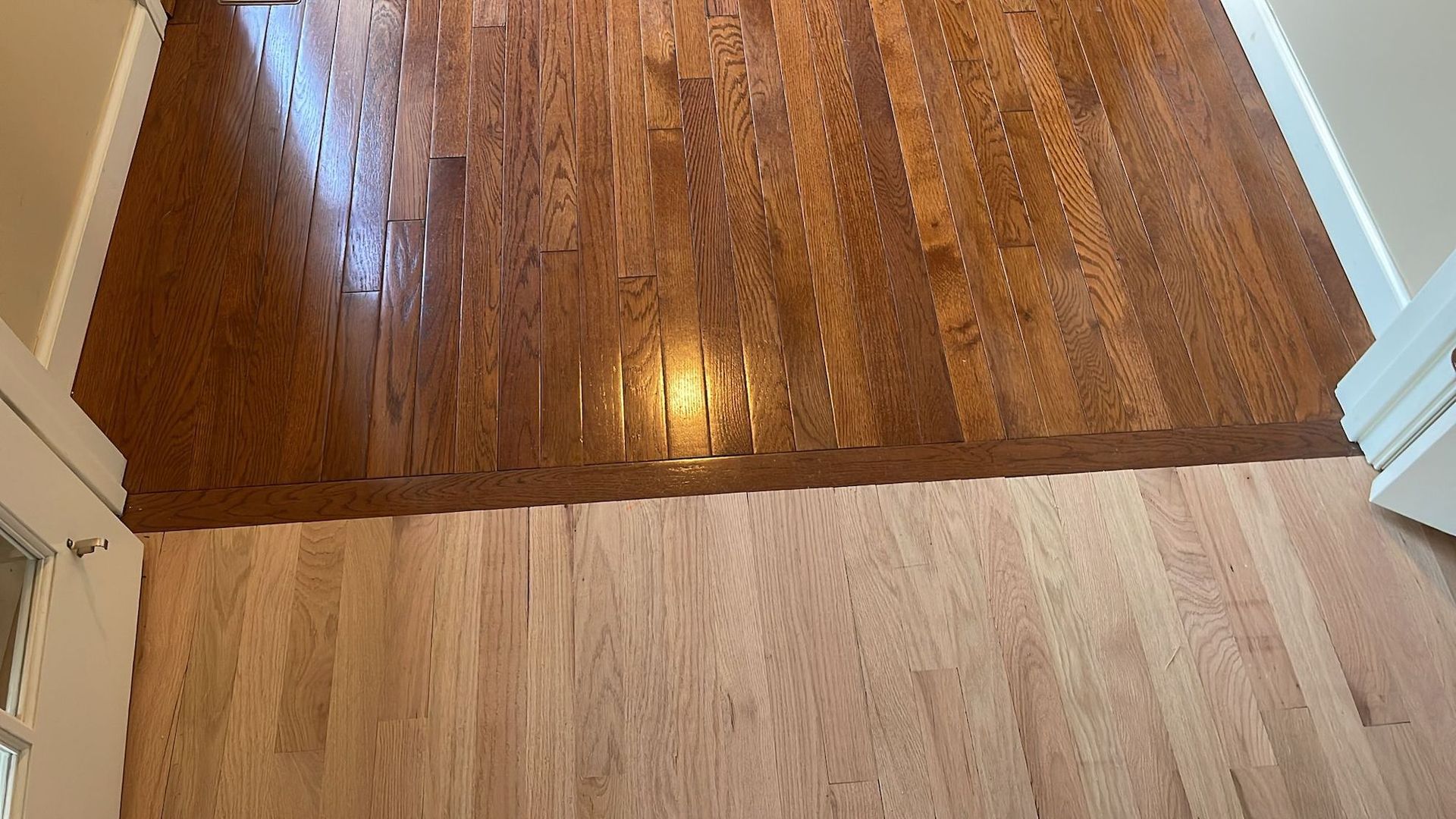 Wooden floors, light and dark brown, meet in a doorway, with a light shining on them.