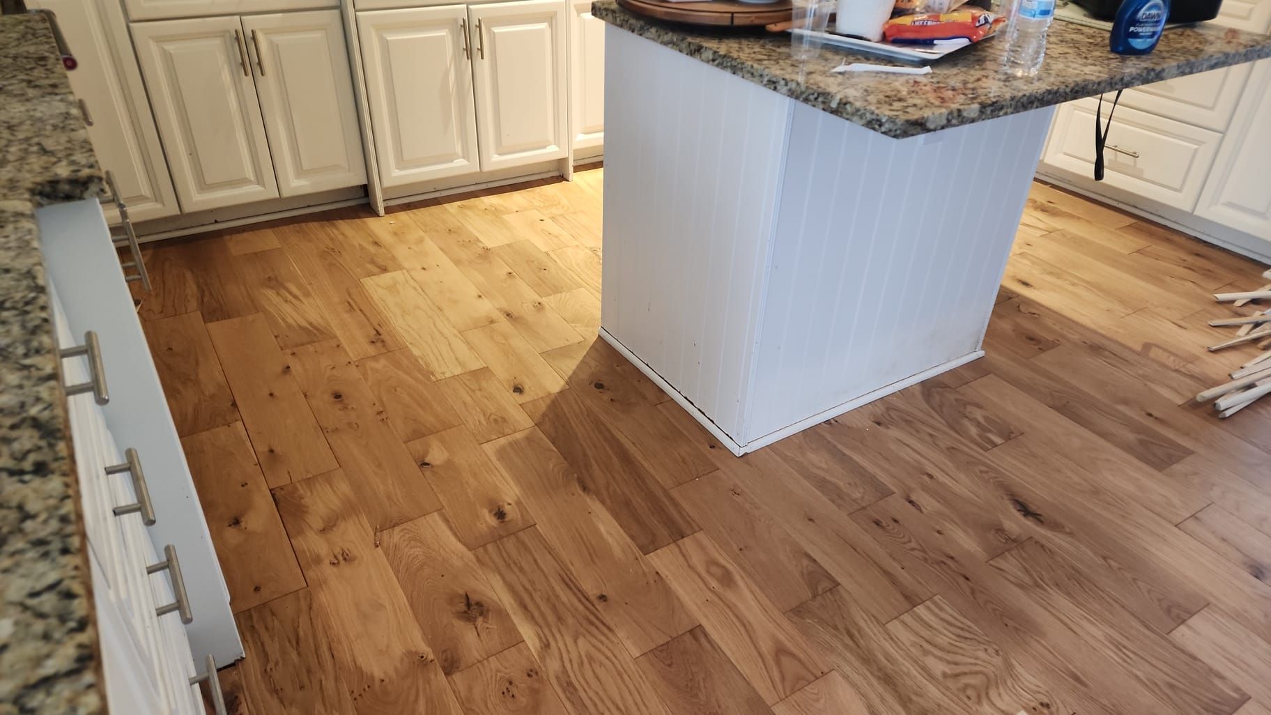 Hardwood flooring in a kitchen with white cabinets and island. Brown granite countertop.