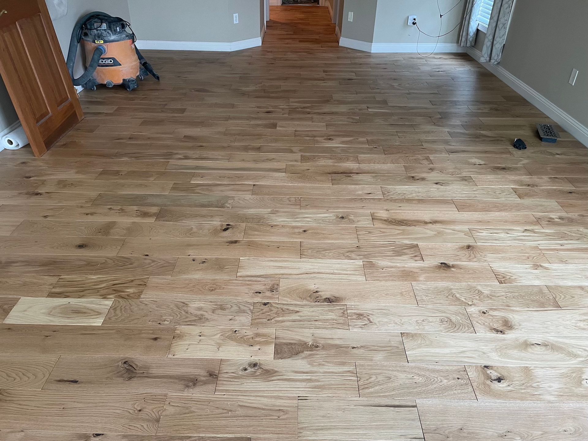 Newly installed light brown hardwood flooring in a room with a door, shop vacuum, and walls.
