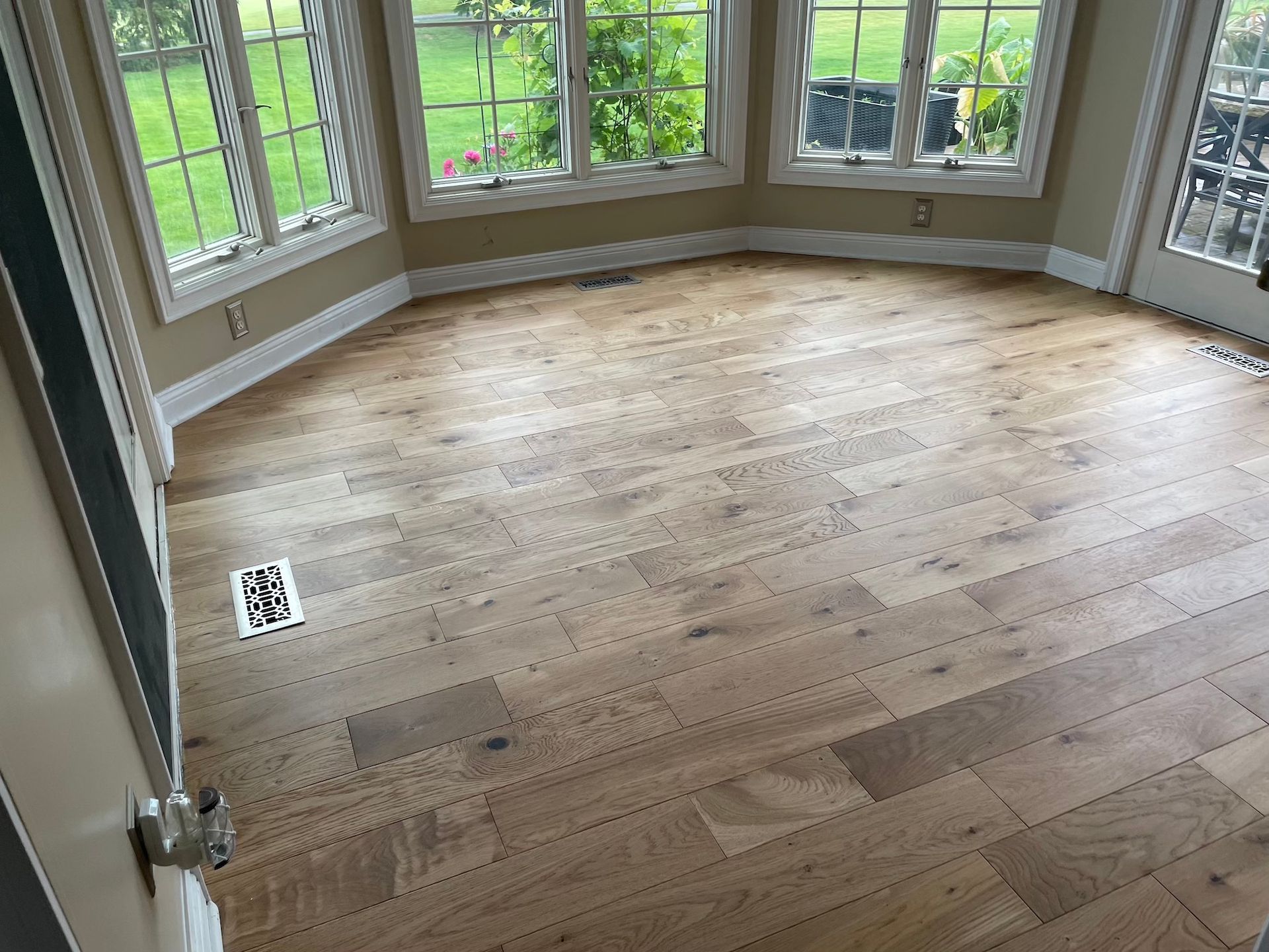 Light wood floor in a sunroom with arched windows and a door.