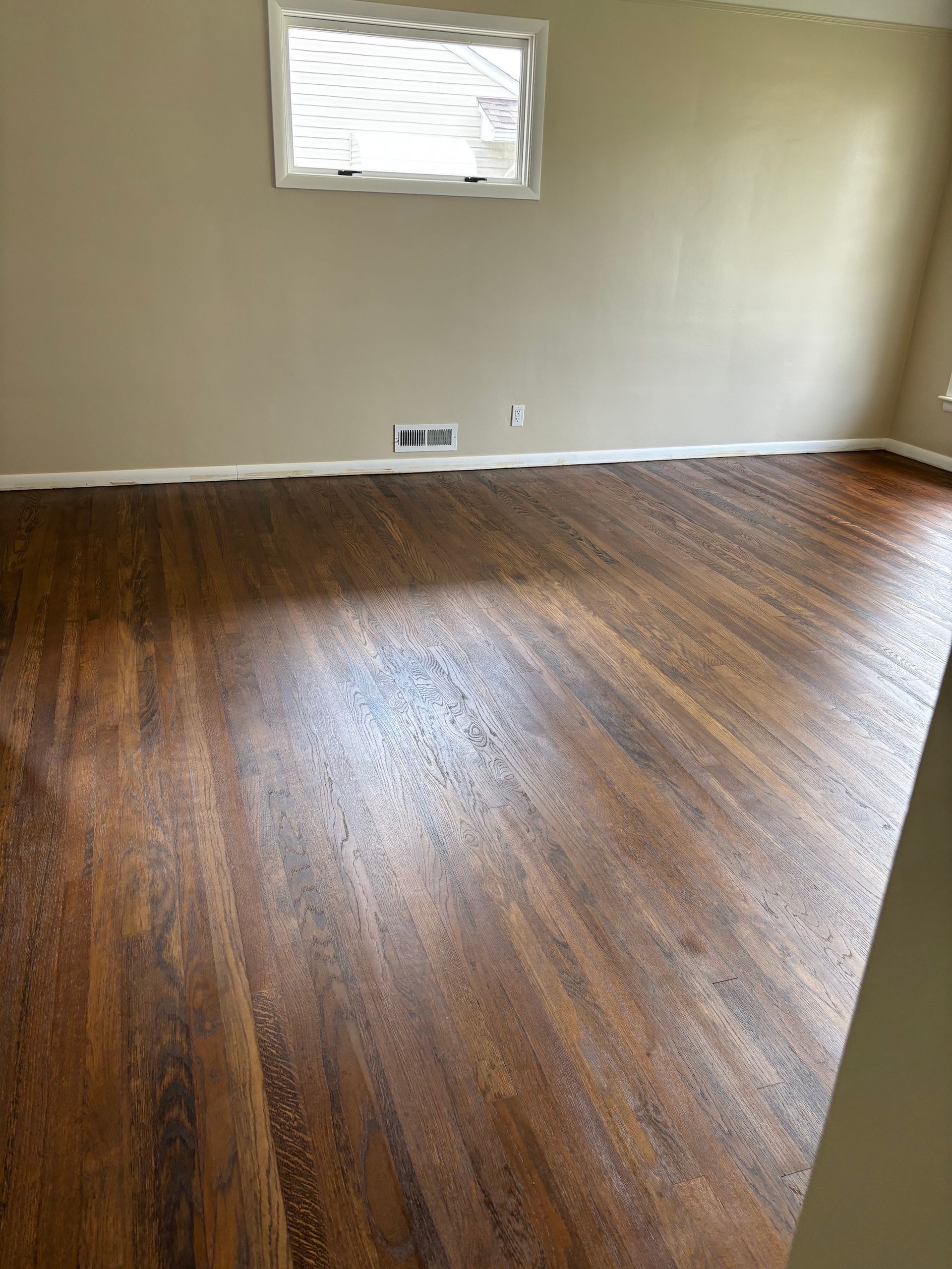 Dark wood floor in room with tan walls, white trim, and a window.