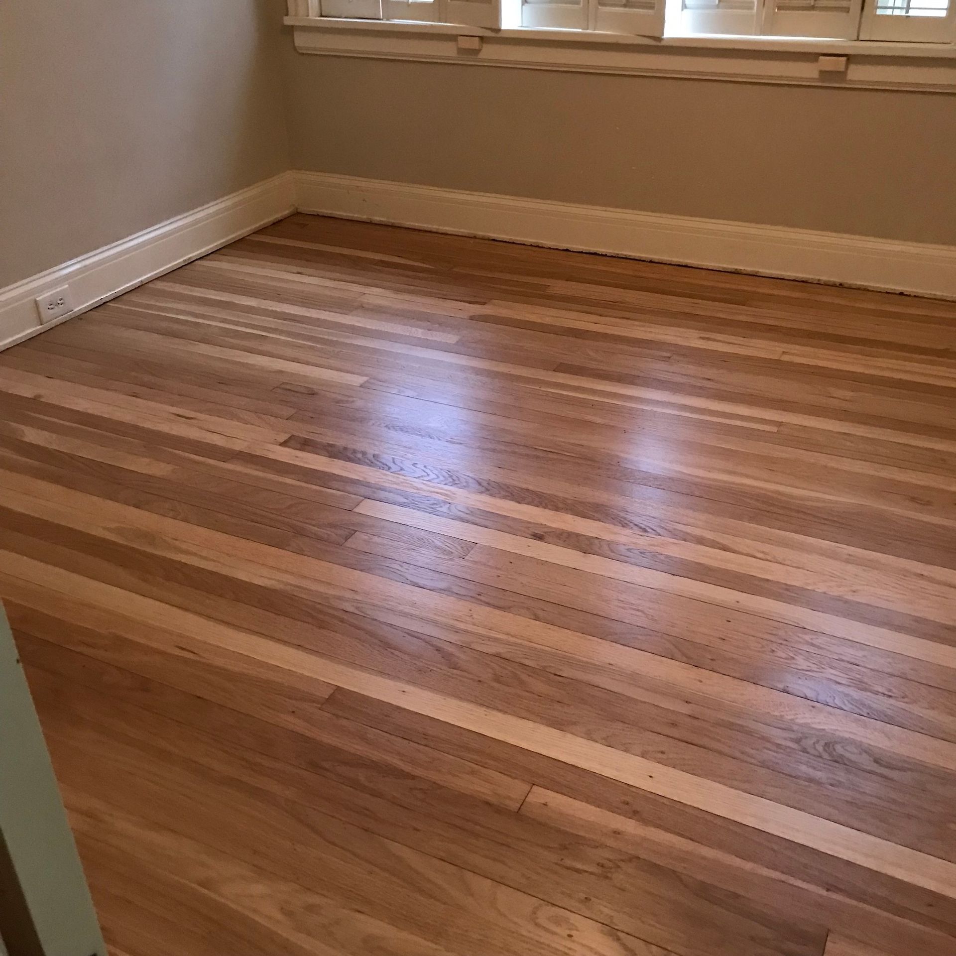 Hardwood floor with alternating light and dark wood planks in a room with a window.