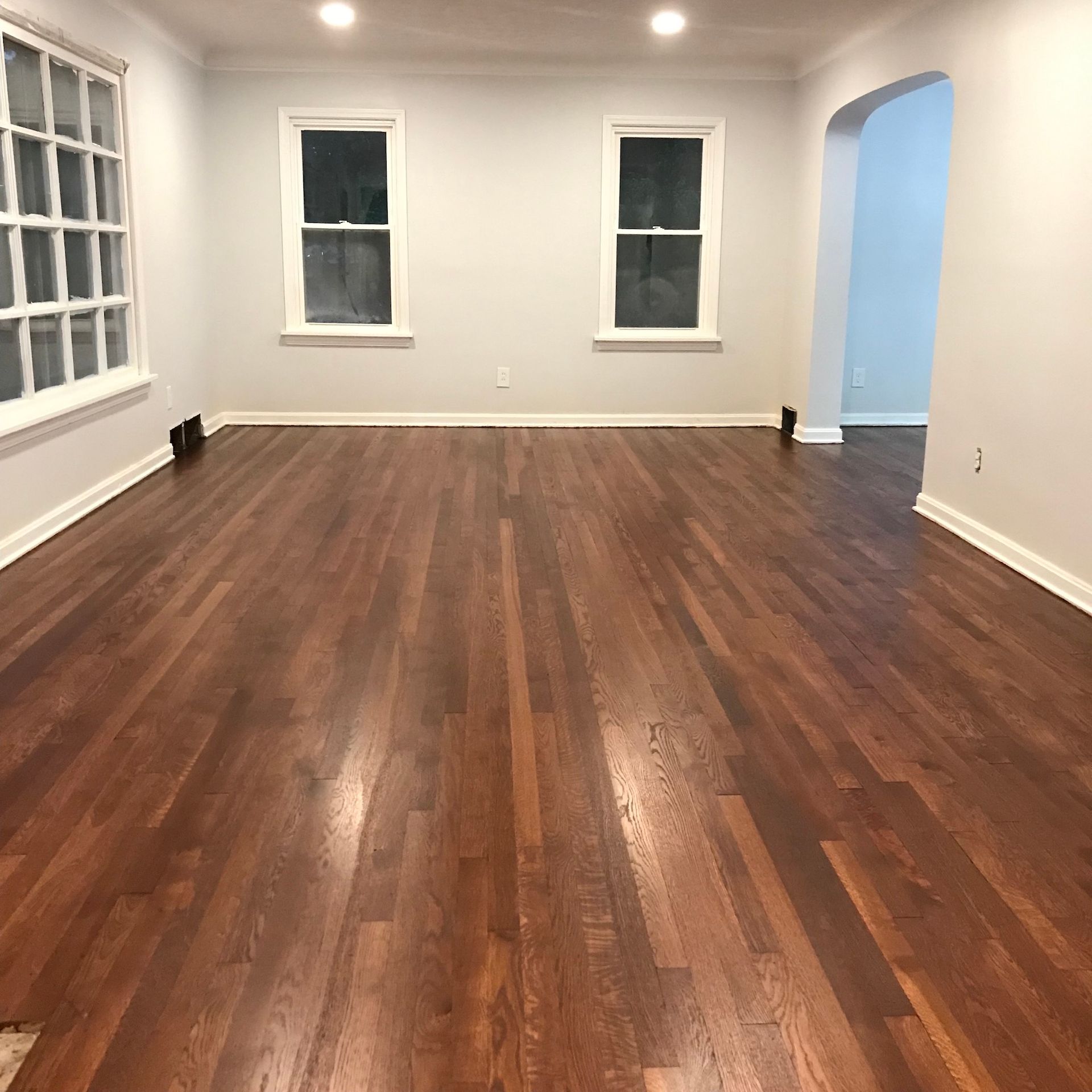 Empty room with newly finished dark wood floors, light gray walls, and white trim.