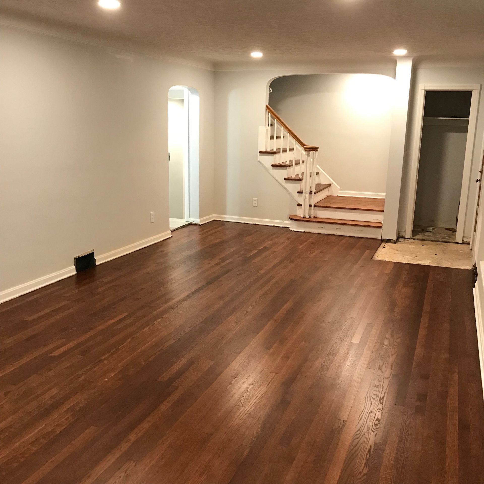 Empty living room with hardwood floors, stairs, and a doorway.