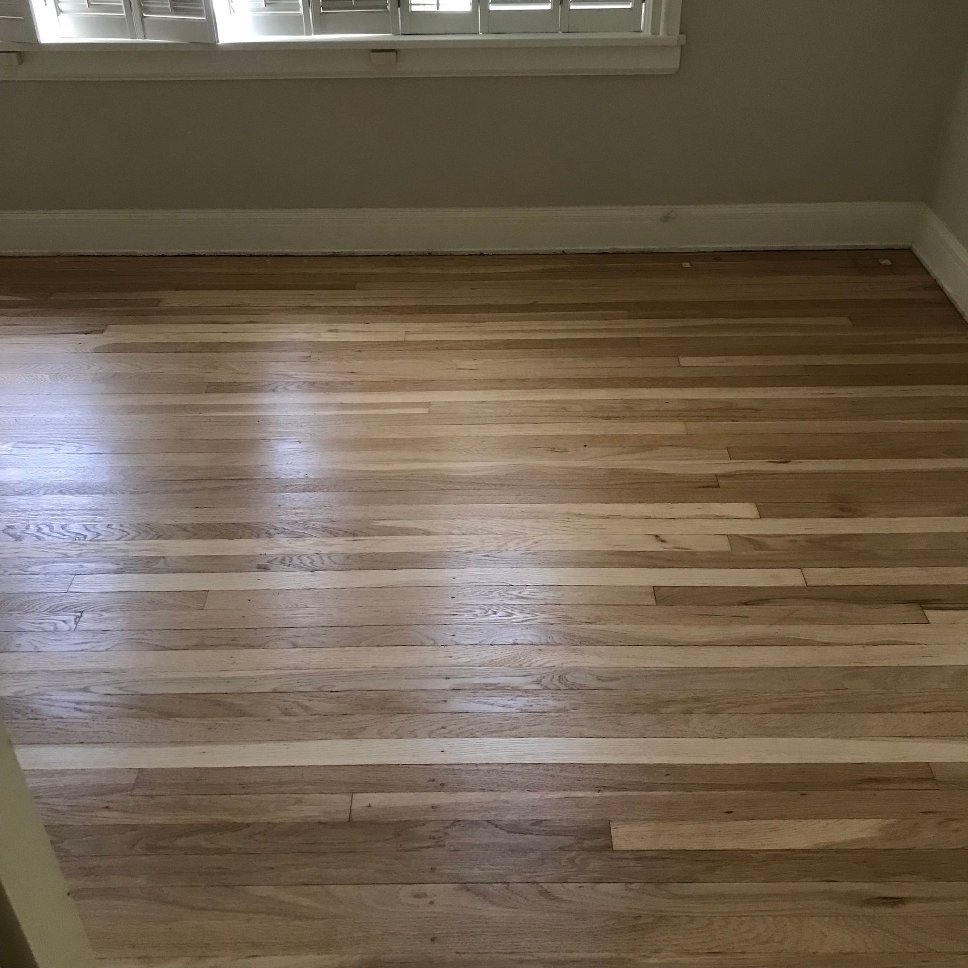 Hardwood floor in a room with a window and baseboards; light brown wood.