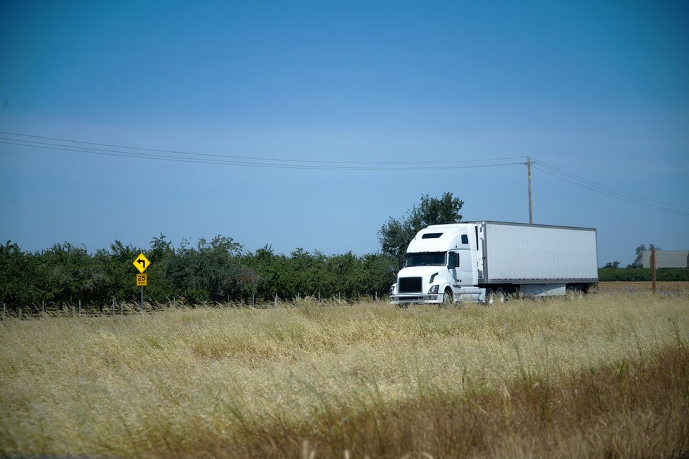 White Semi-truck Drives on a Rural Road Next to Tall Grass — Mission Truck Training in Caloundra, QLD