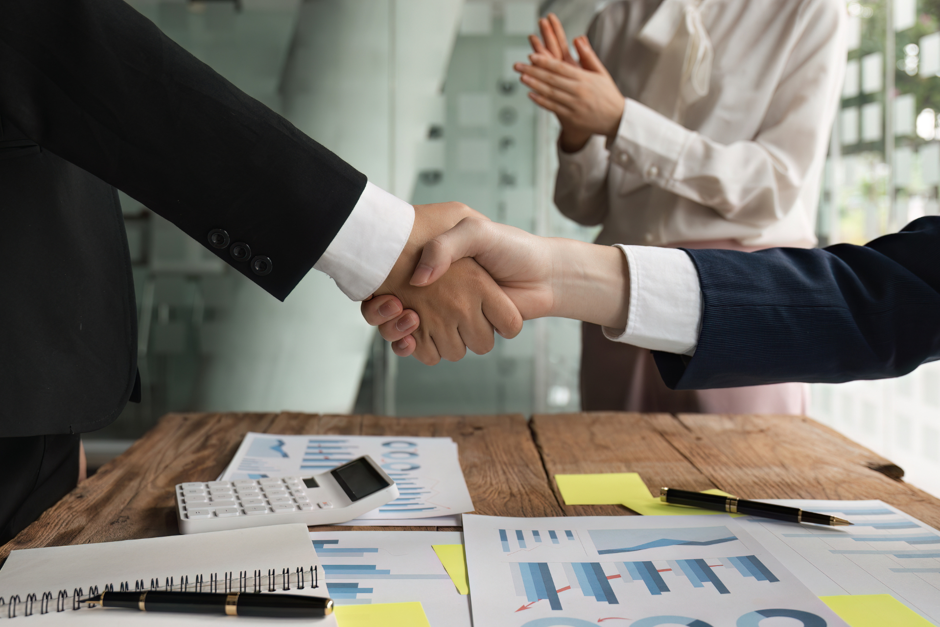 Two business people are shaking hands over a wooden table.