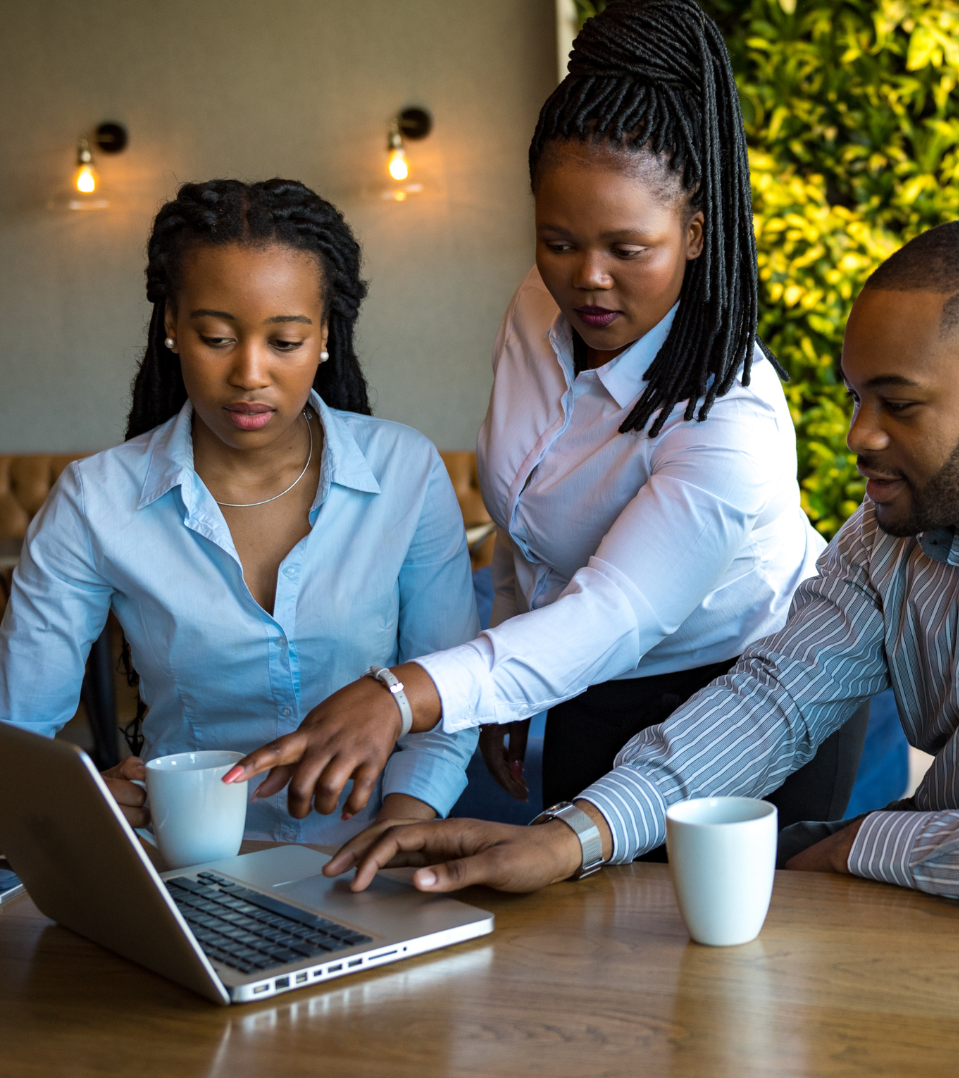 A group of people are sitting at a table looking at a laptop computer.