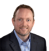 A man in a suit and blue shirt is smiling for the camera.