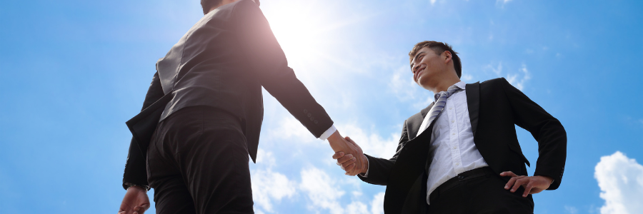 Two businessmen are shaking hands in front of a blue sky.