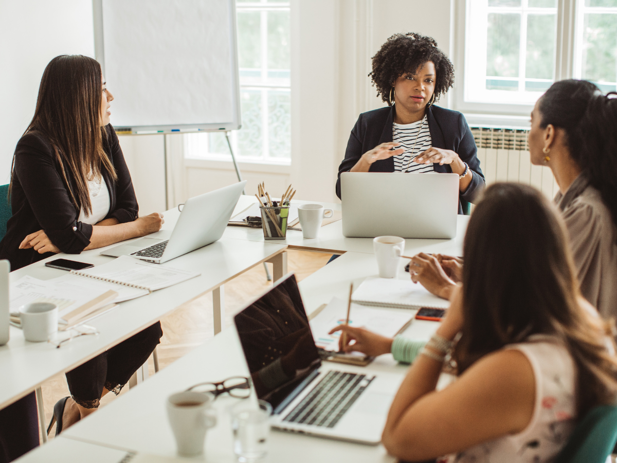 A group of women are sitting around a table with laptops.