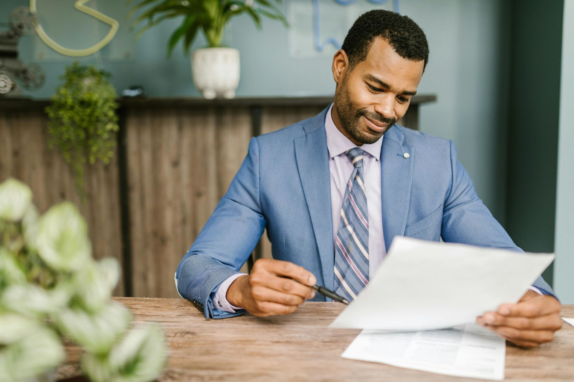 A man in a suit and tie is sitting at a table reading a piece of paper.