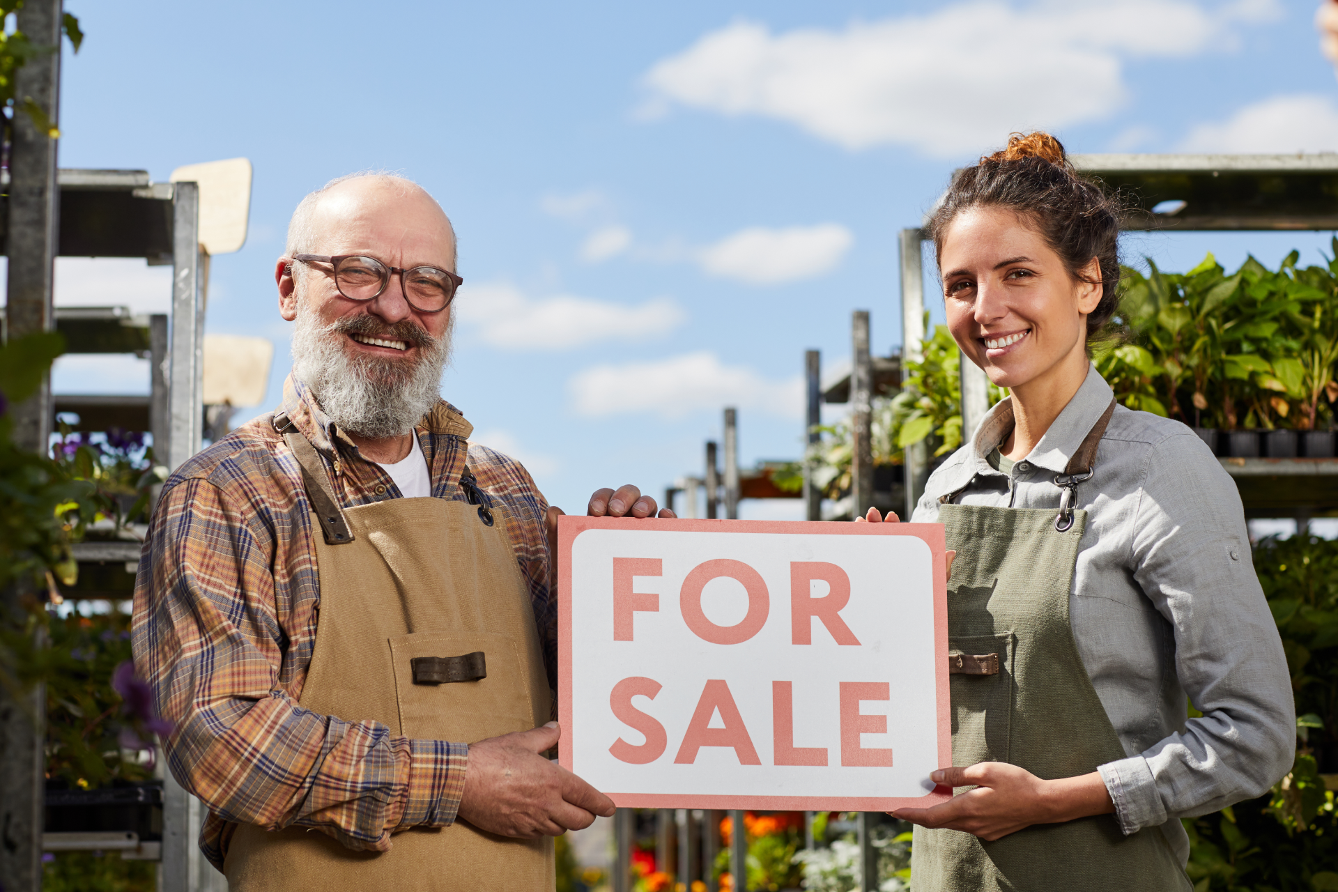 A man and a woman are holding a for sale sign in a garden center.