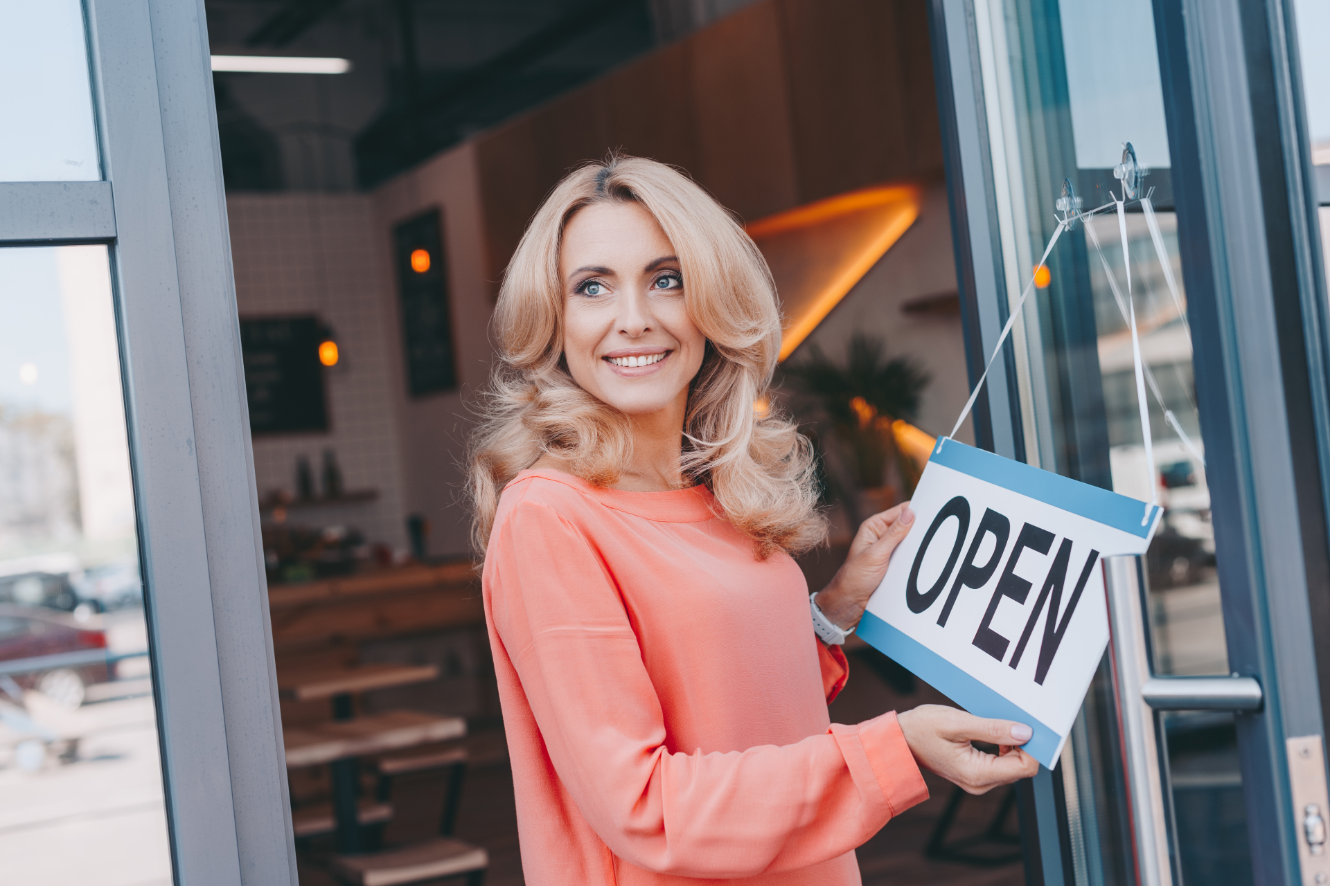 A woman is holding an open sign in front of a store door.