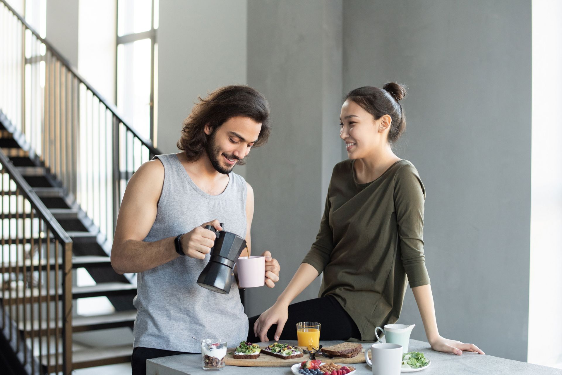 Two people chatting by a table, one pouring from a bottle and the other smiling in a modern loft space