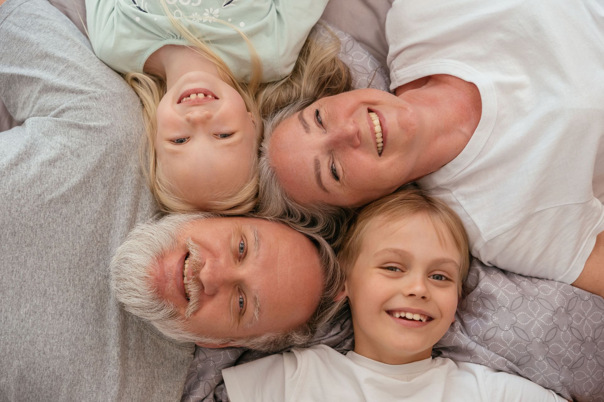 Family of four lying head-to-head on a bed, smiling at the camera.