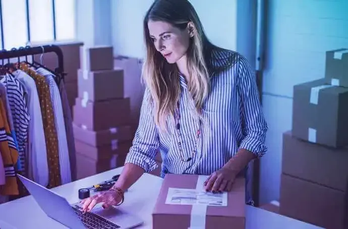 A woman is sitting at a table with a laptop and a box.