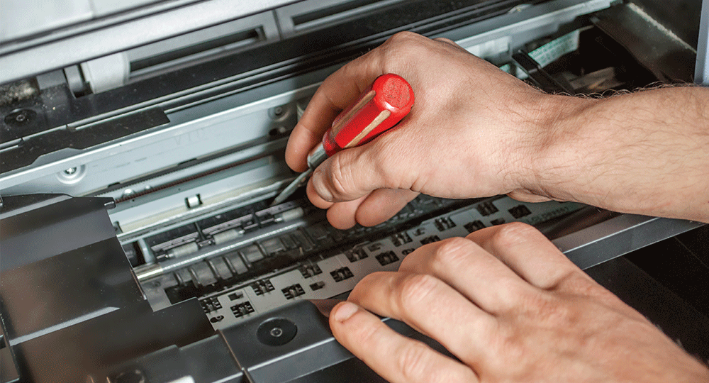 A person is fixing a printer with a screwdriver.