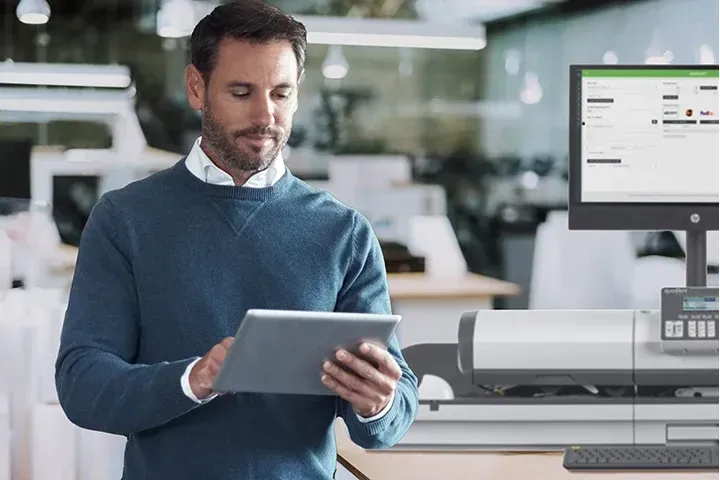 A man is holding a tablet in front of a computer.