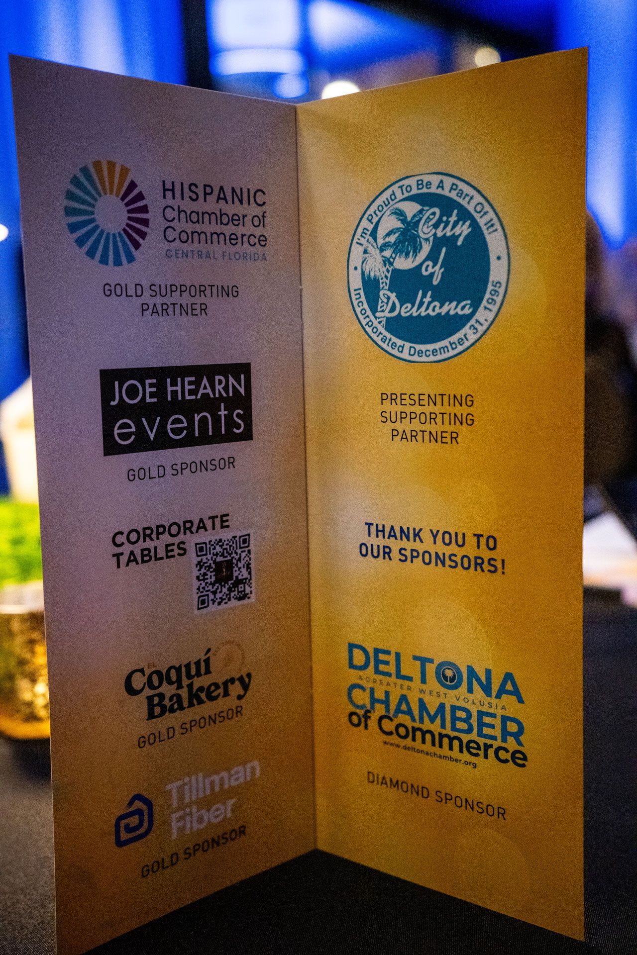 Gold event brochure with sponsor logos, including Deltona Chamber of Commerce, on a textured blue background