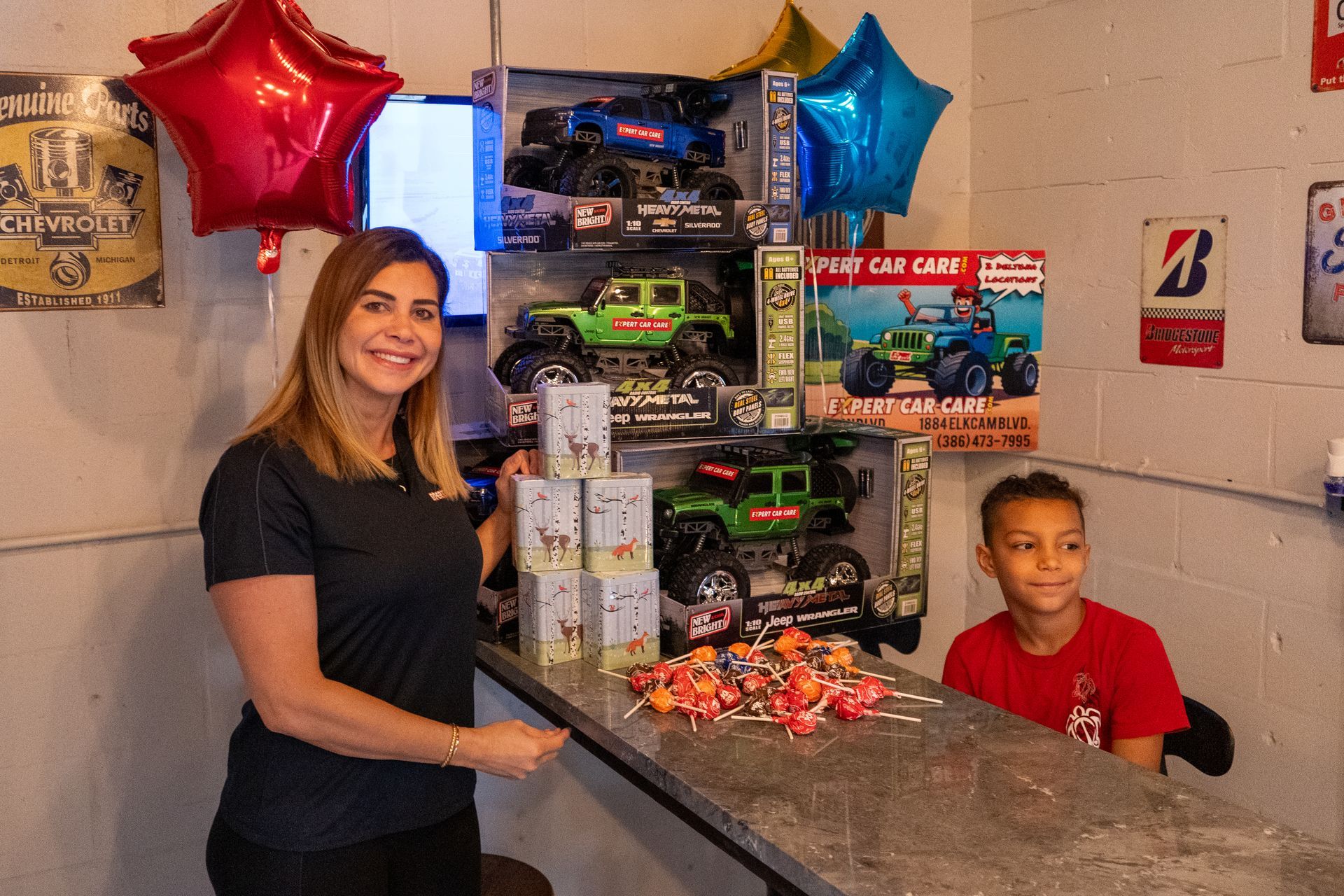 Woman and child behind a counter with toy cars and balloons in a small shop or party display
