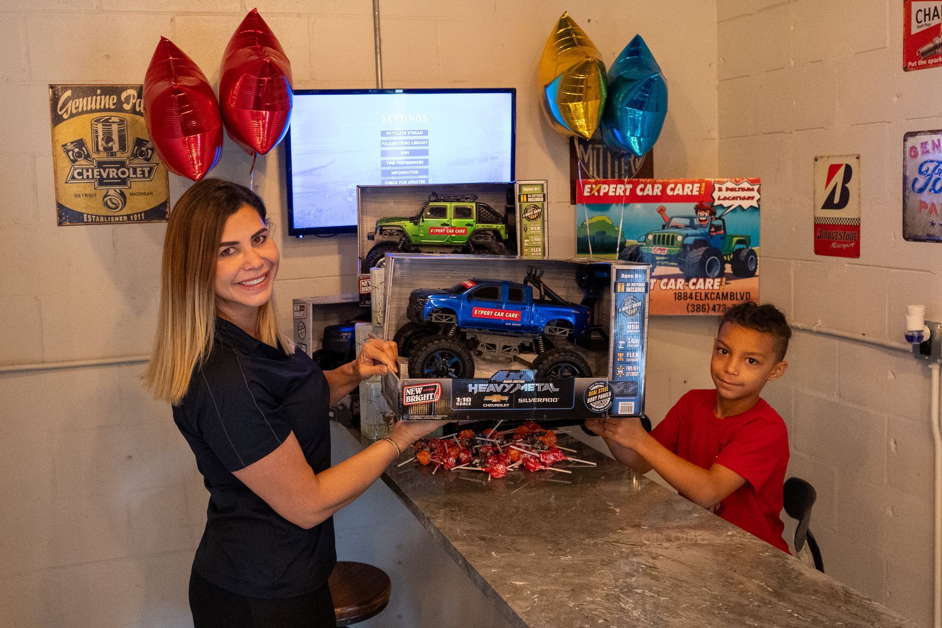 Woman and child at a counter holding a toy car box with balloons in the background