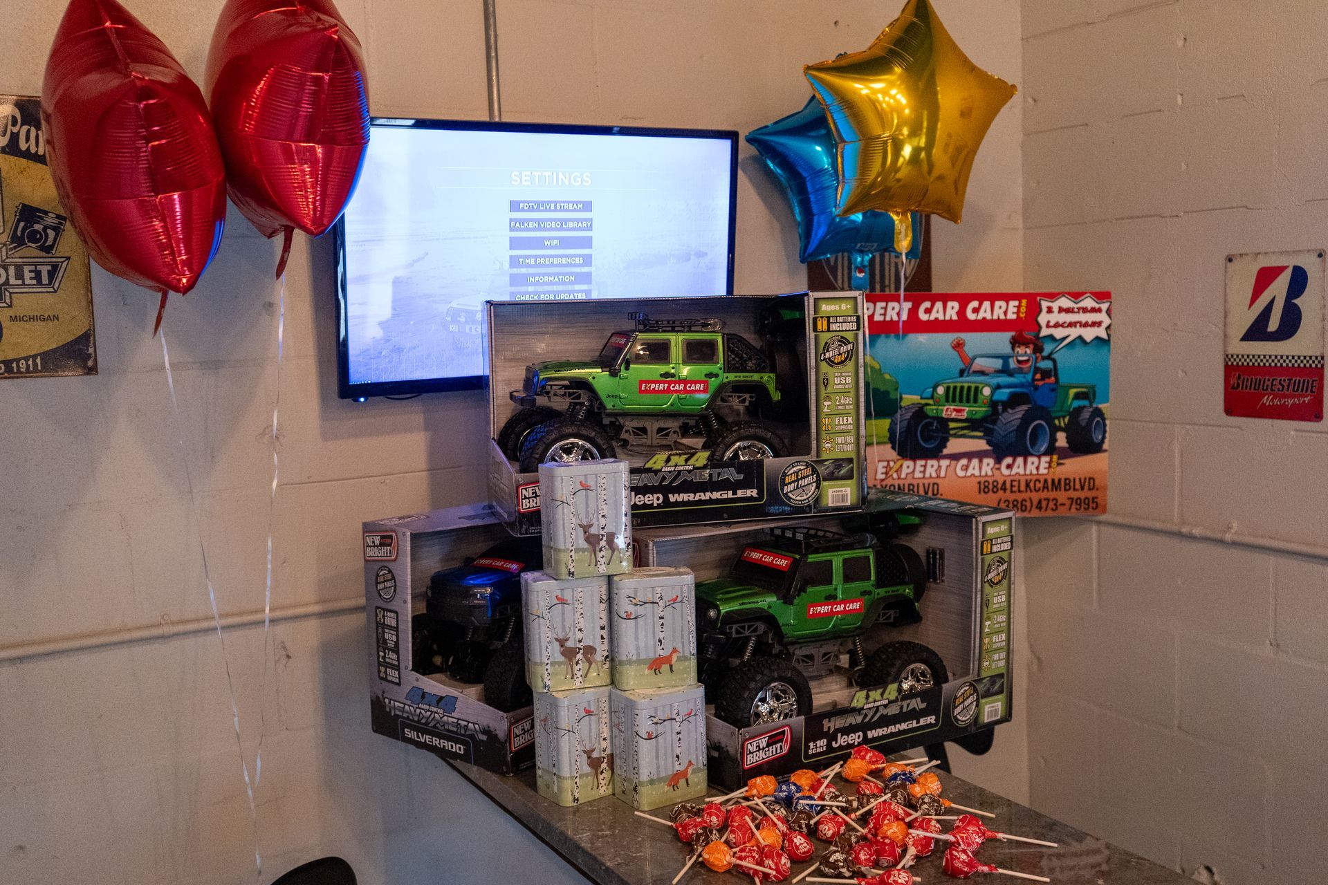 Table display of toy monster trucks and gift stacks with balloons in a store or event setting