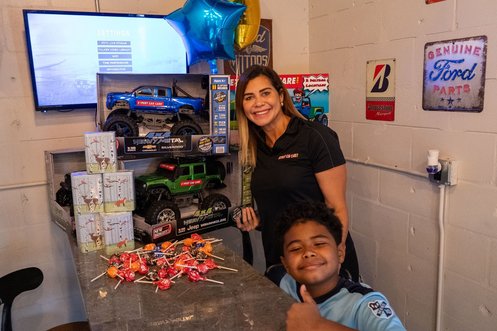 Woman and child posing beside a display of toy cars and gift items in a shop-like room
