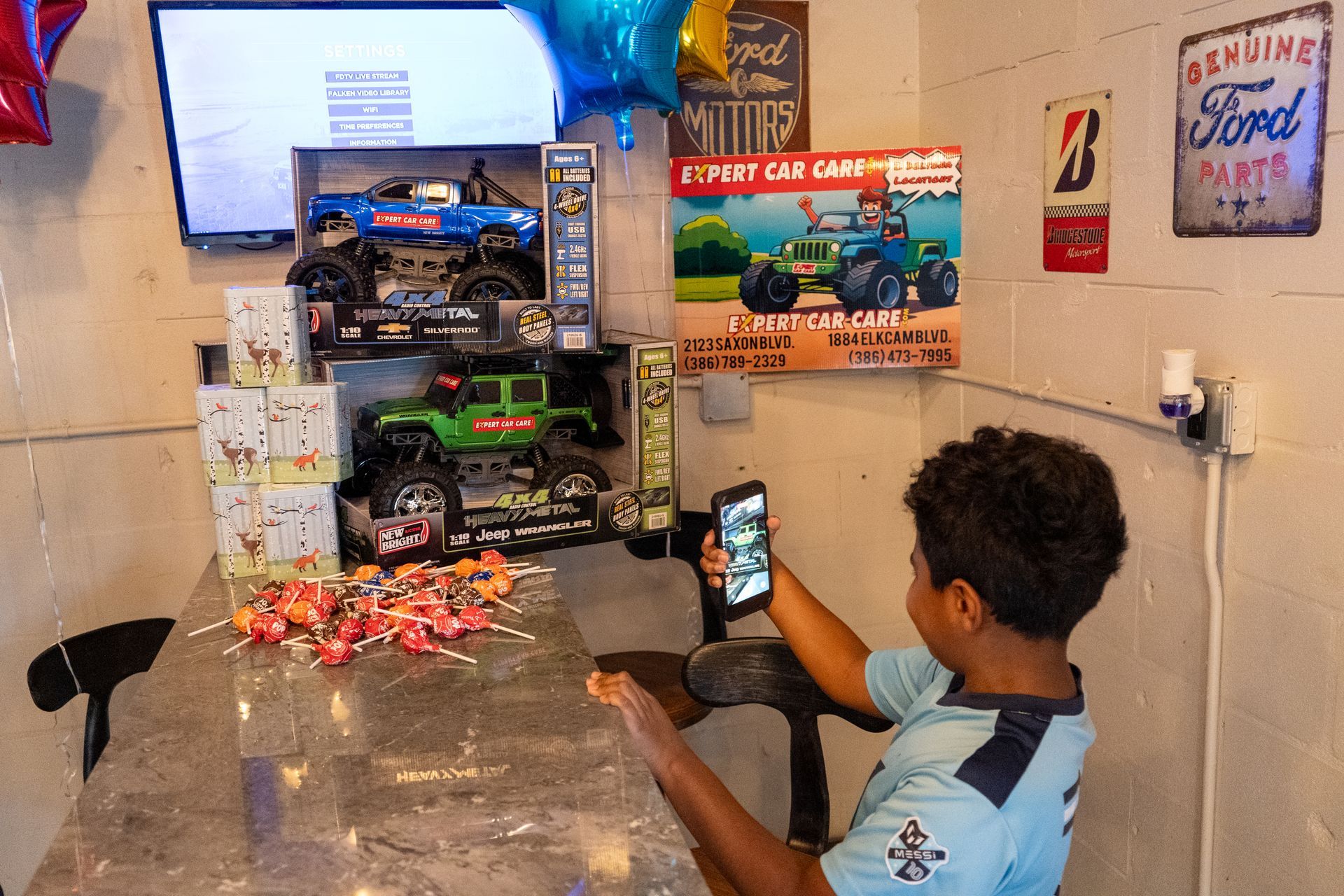 Person using a smartphone beside a toy truck display in a small room with posters and a TV