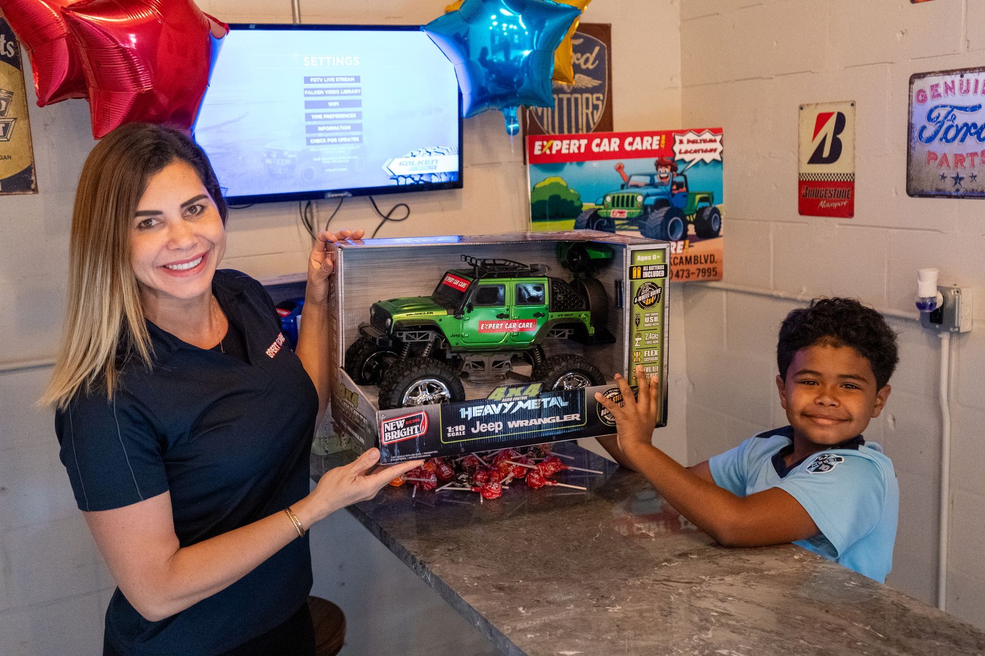 Woman and child presenting a green toy car gift in a decorated room, both smiling at the camera