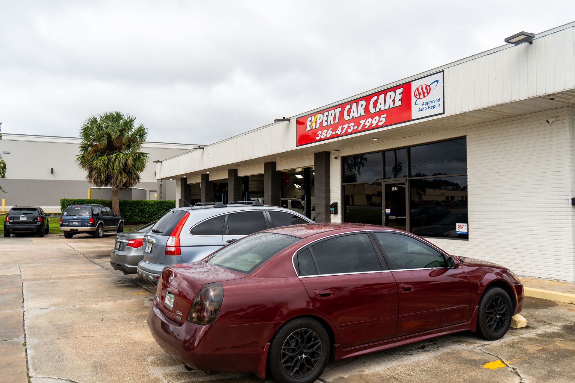 Auto repair shop storefront with parked cars in front, including a burgundy sedan and silver SUV.