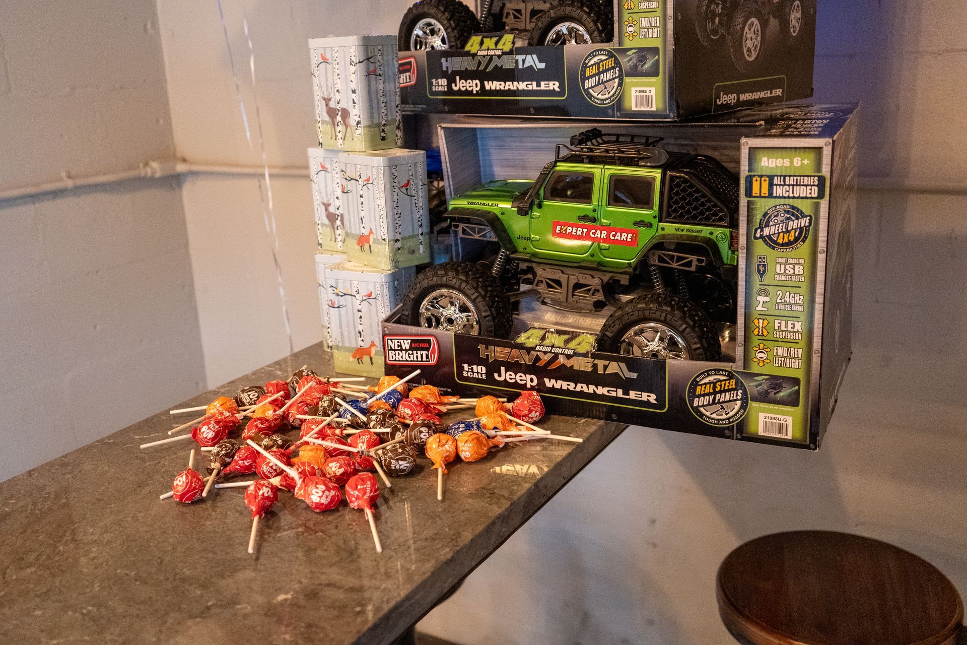 A pile of candy bars and a green toy monster truck on a counter, with stacked boxes in the background