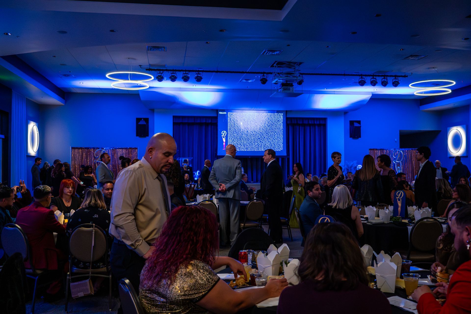 People seated at tables in a blue-lit banquet hall during a social gathering