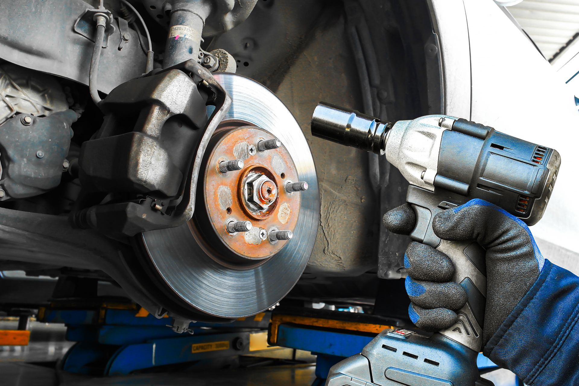 Mechanic using a cordless impact wrench on a car brake rotor in a garage