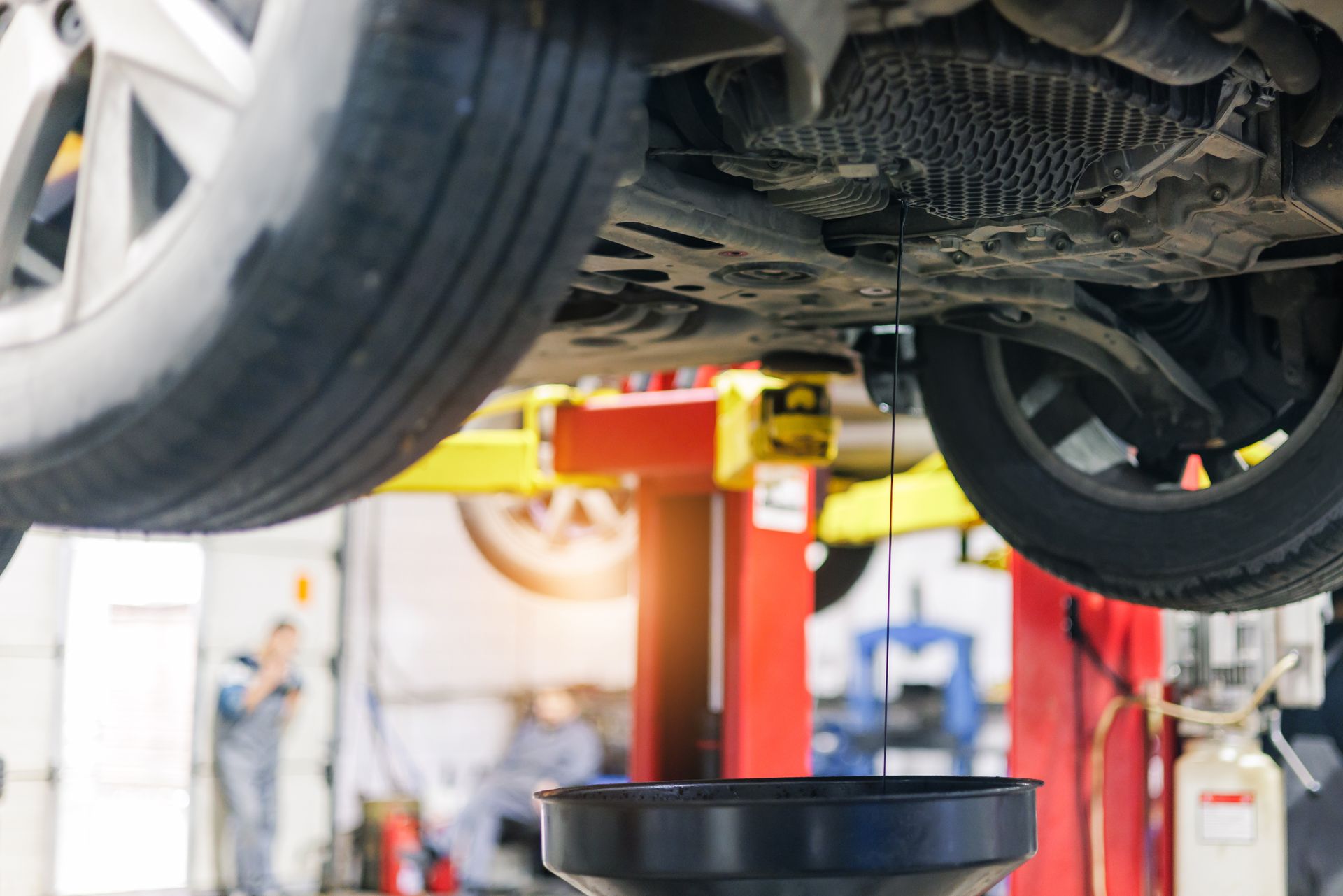 Car on a lift in an auto repair shop, with a drain pan positioned underneath.