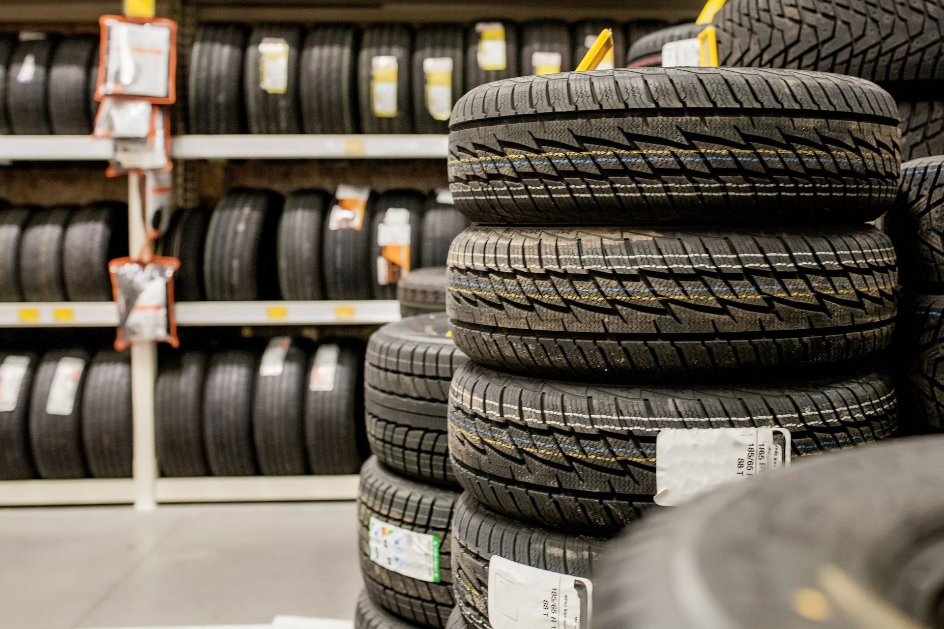 Stacked tires displayed in a tire shop aisle, with shelves of tires in the background.