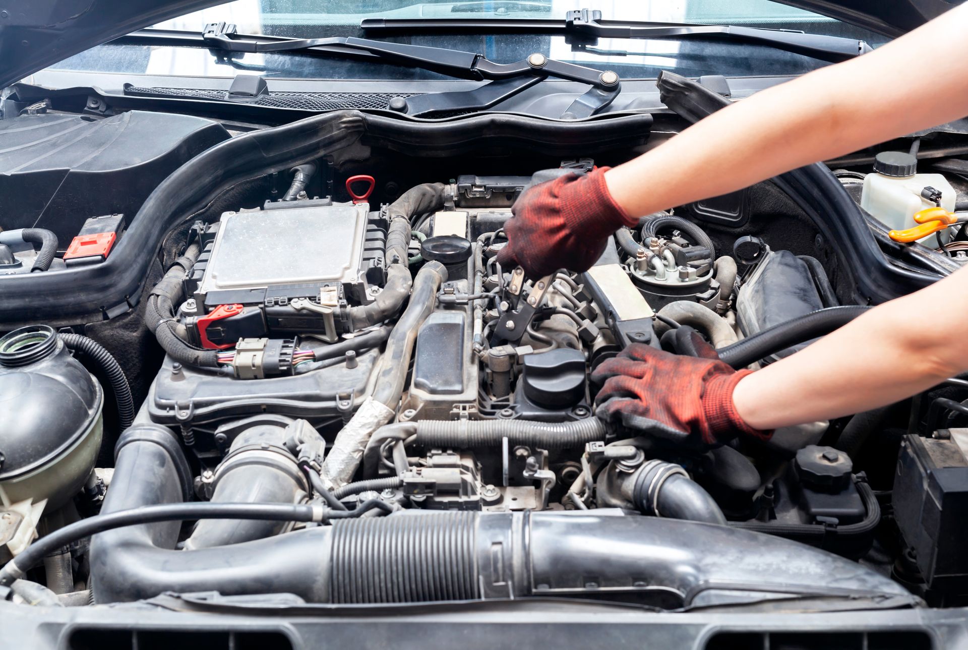 Mechanic’s gloved hands working on a car engine in an open hood compartment