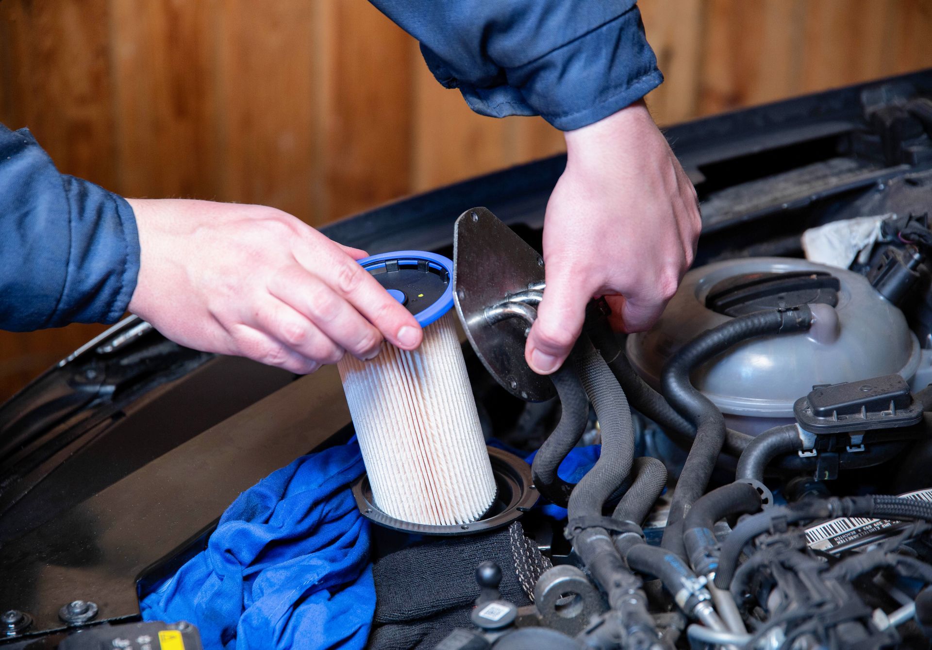 Hands working in a car engine bay, holding a filter and blue hose near the radiator.