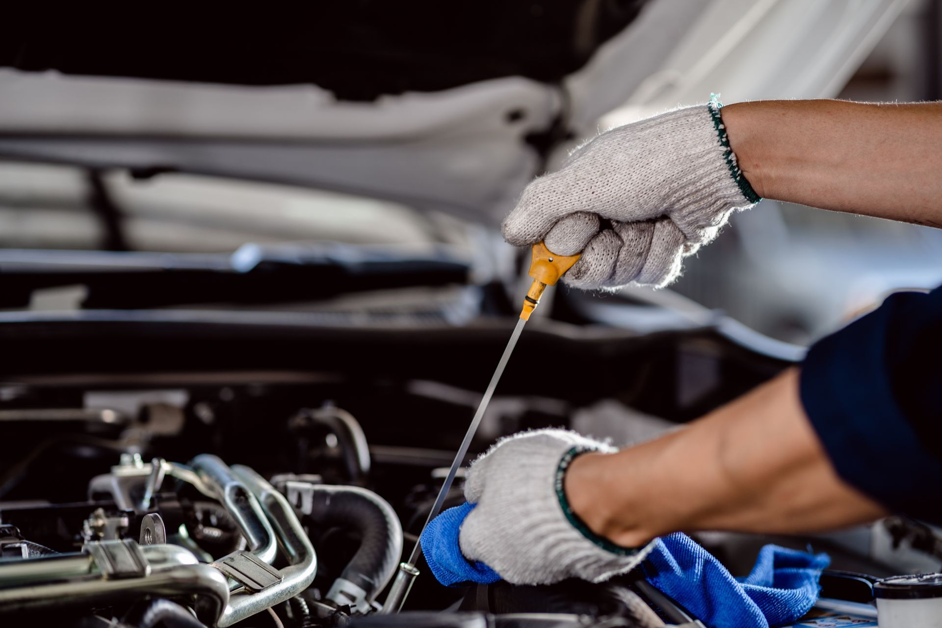 Mechanic in gloves checking engine oil level with a dipstick under an open hood