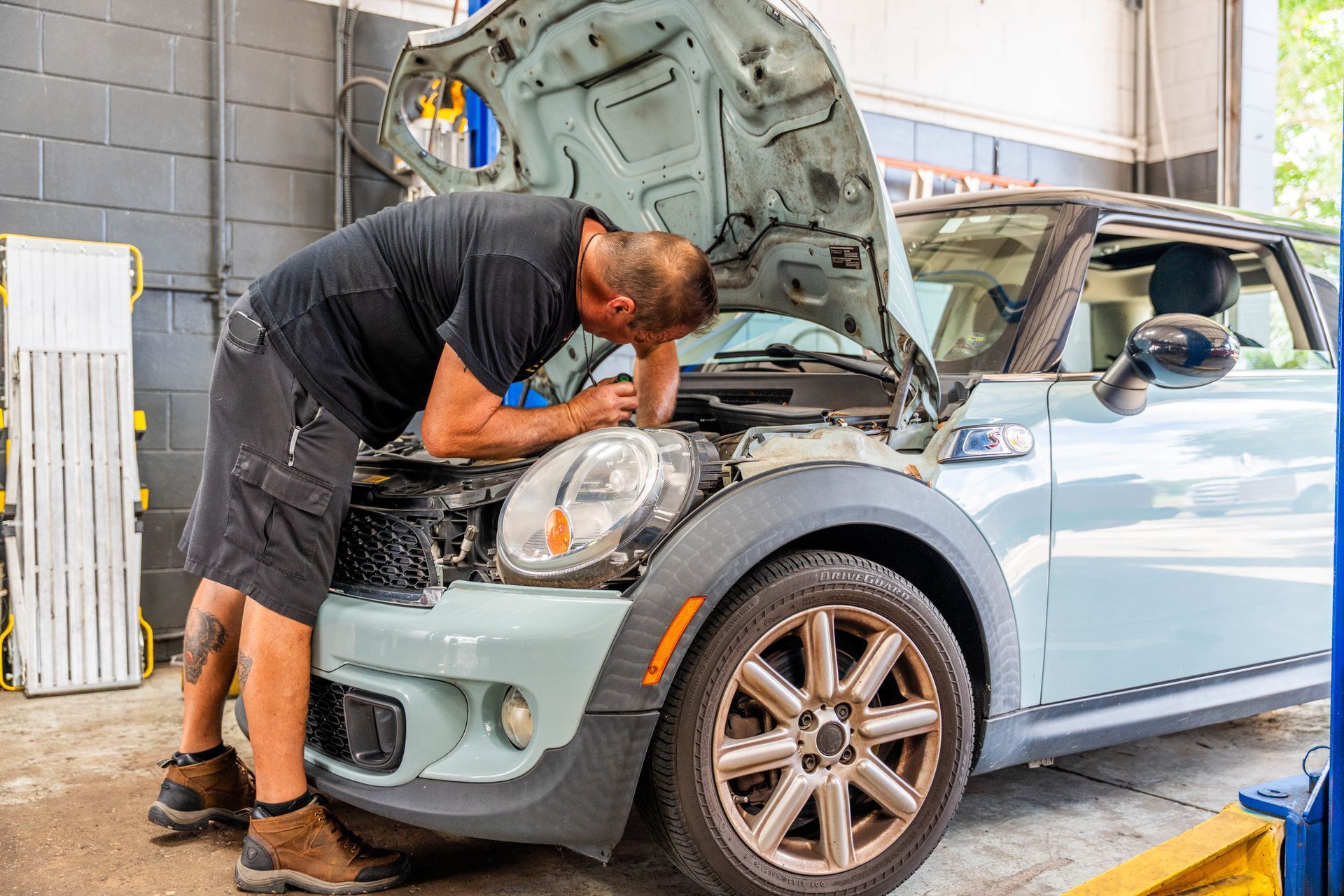Mechanic working under the hood of a light blue Mini Cooper in a garage