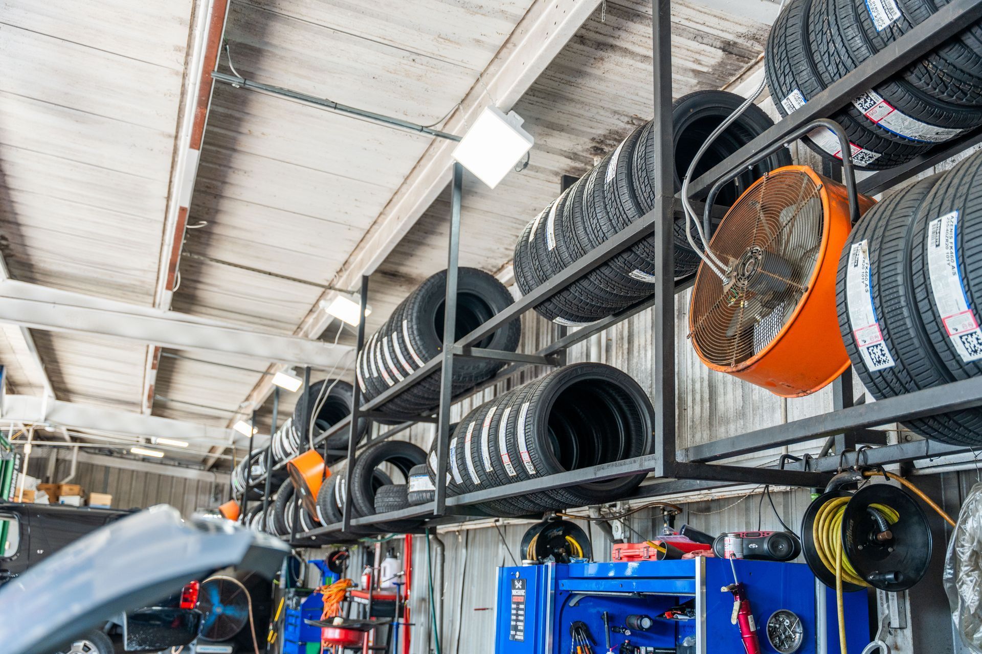 Tire shop wall with stacked tires on shelves and orange fans in a bright garage interior