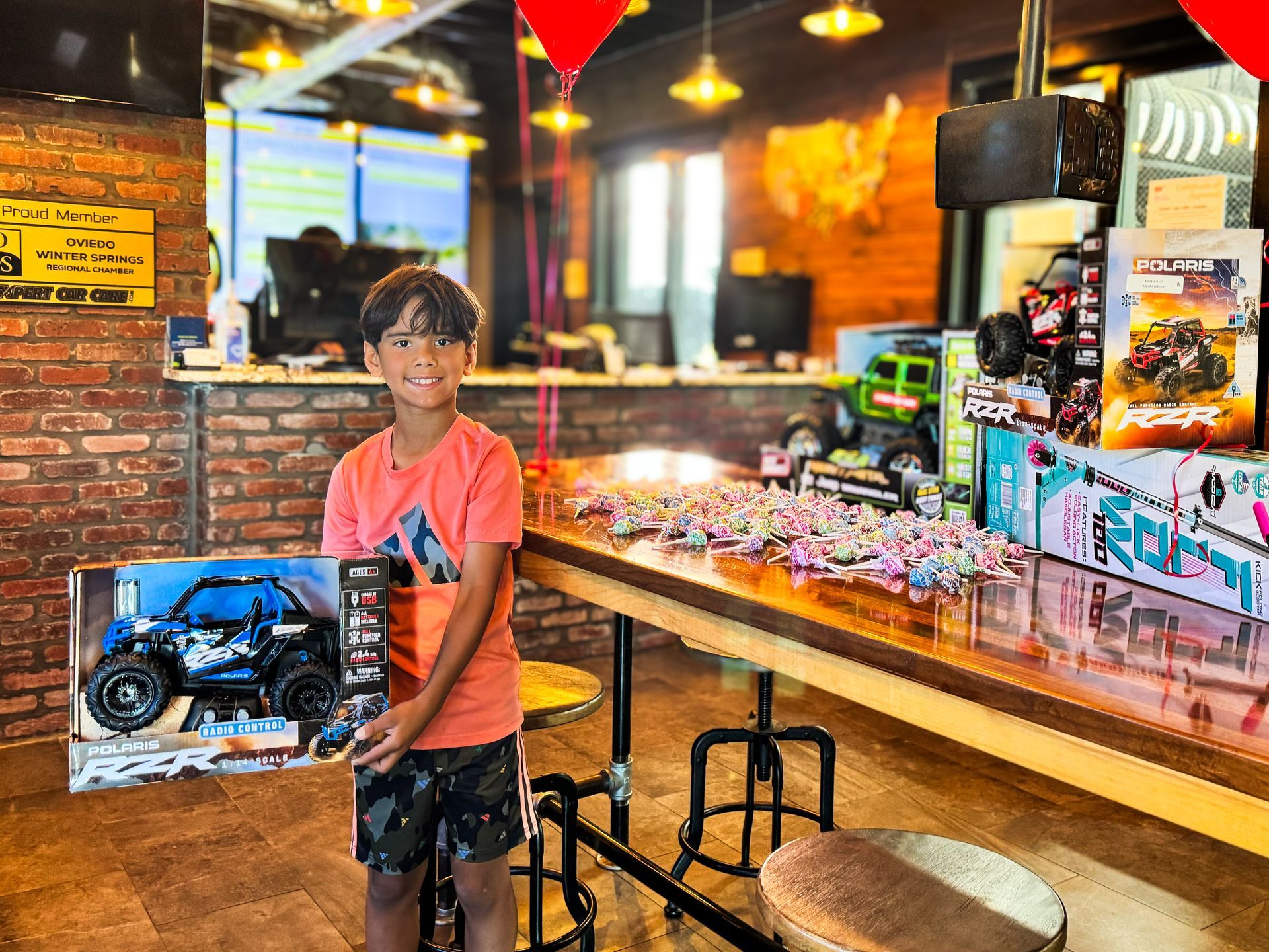 Boy smiling and holding a boxed toy car in a brightly lit restaurant or store interior