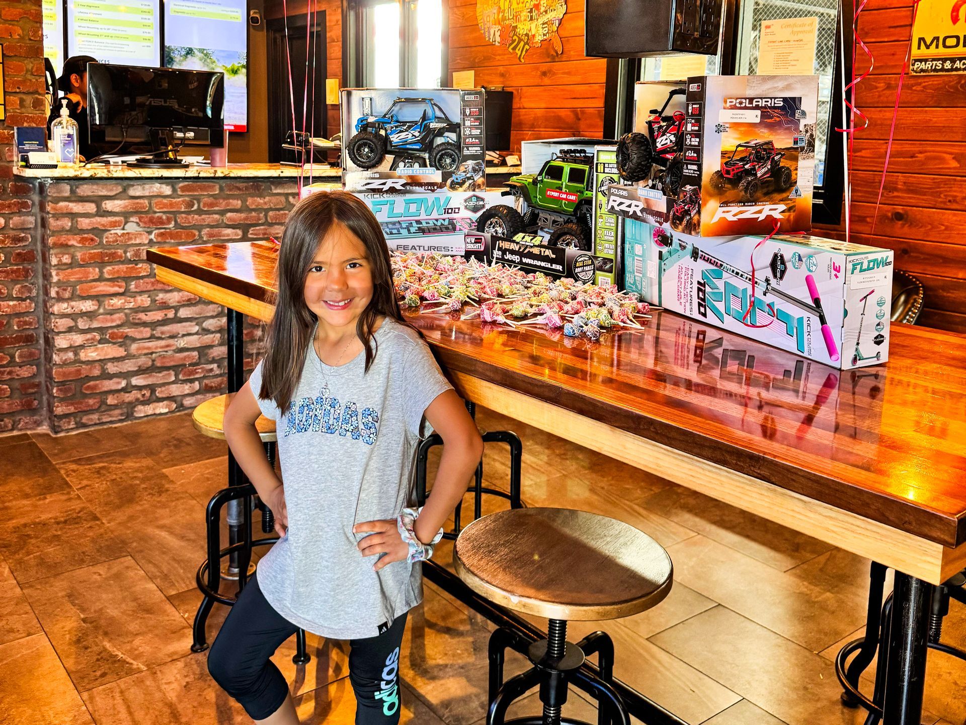 Girl posing beside a long wooden counter in a rustic restaurant, with racing-style displays behind her.