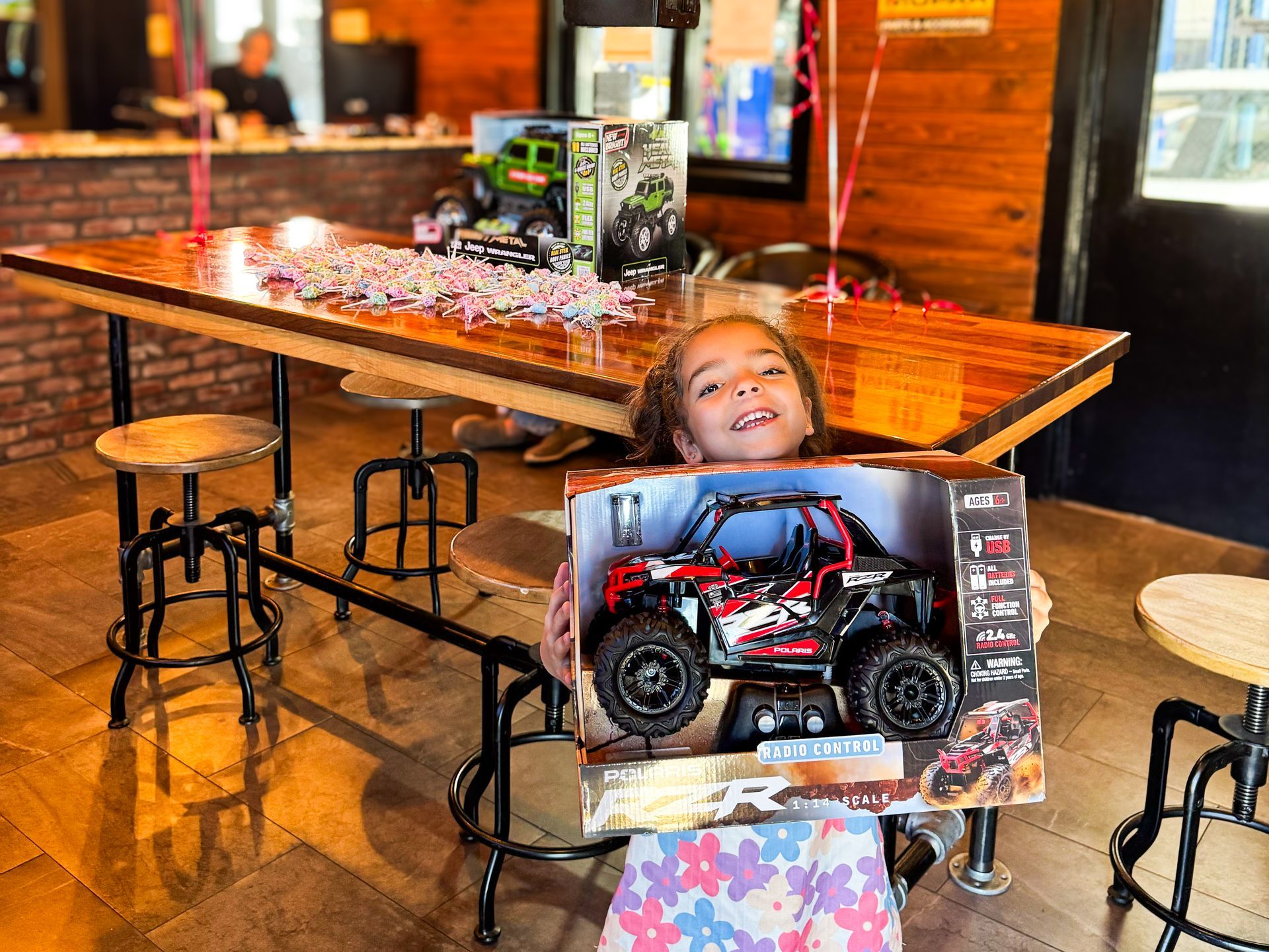 Child holding a boxed toy car in a restaurant, smiling beside a table