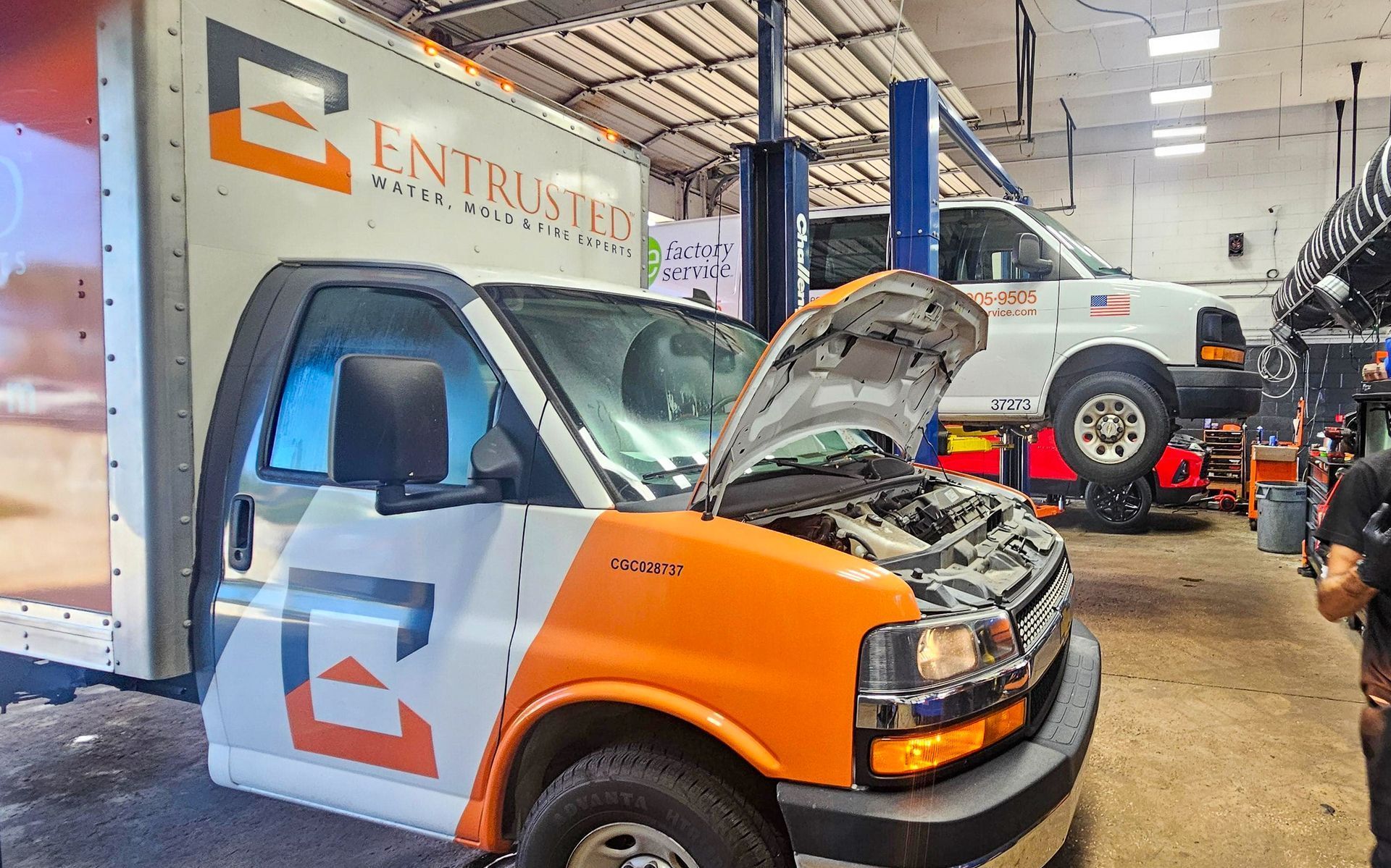 Orange and white service van with hood open in an auto repair shop